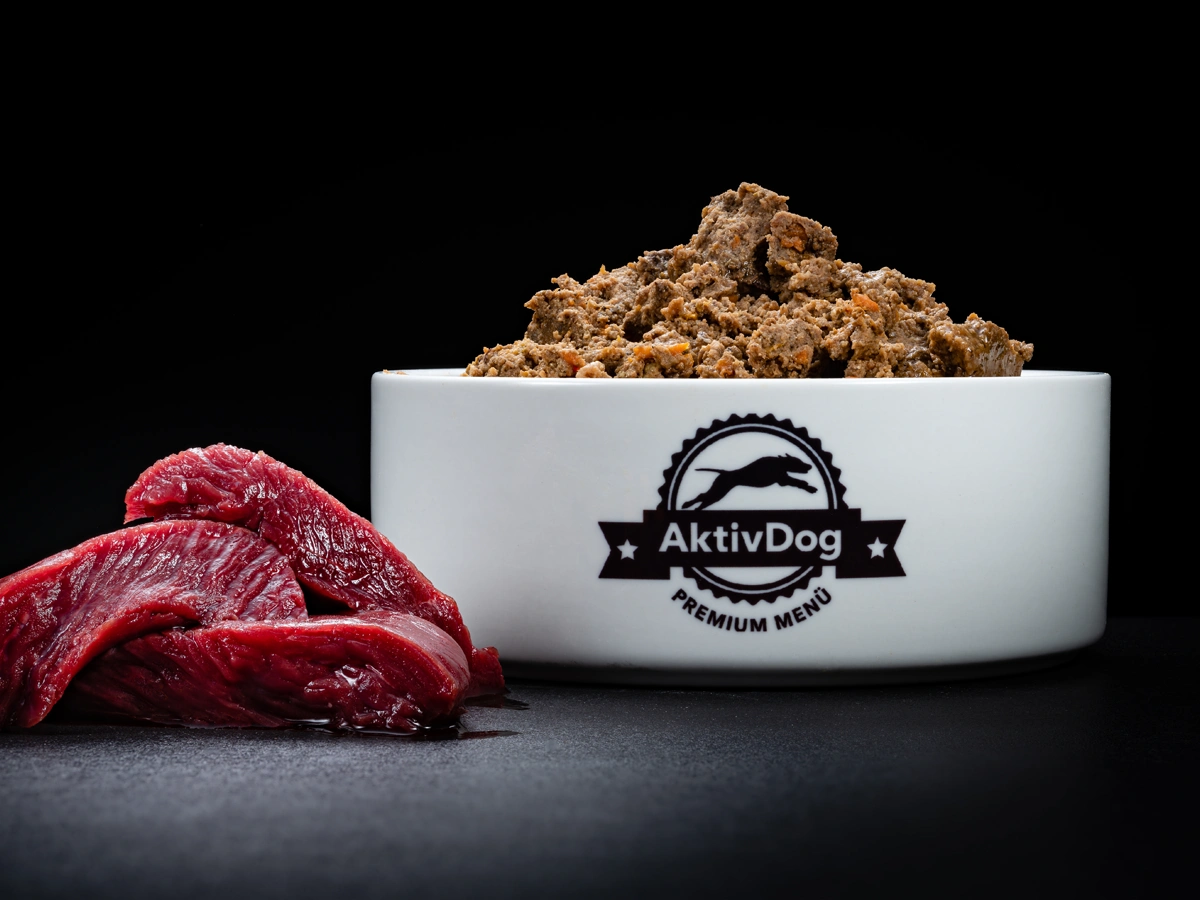 Großaufnahme von AktivDog Hundefutter Rotwild mit links daneben liegendem rohen Hirschfleisch
